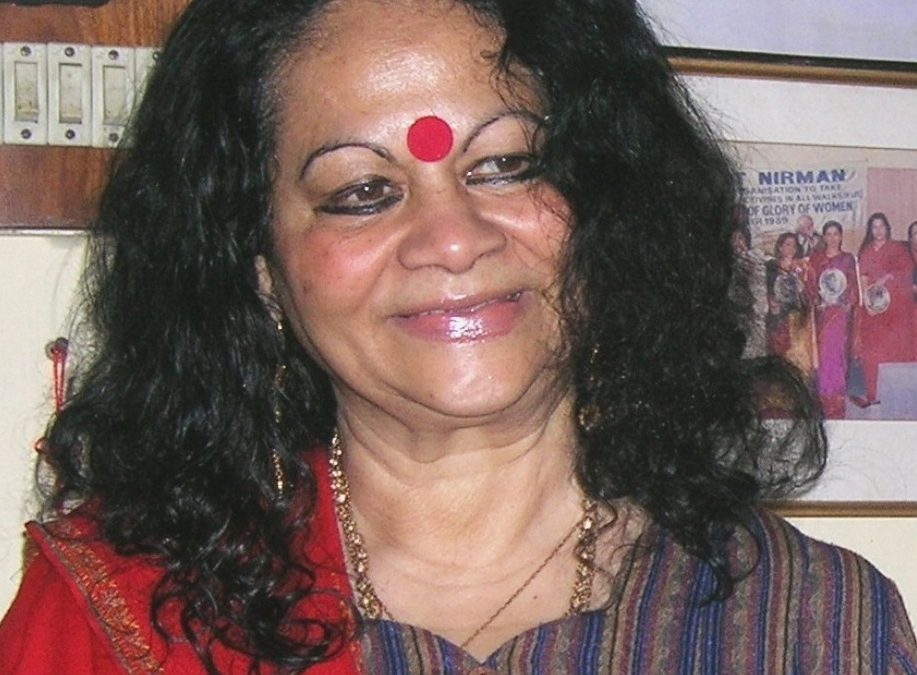 Indira Goswami with long curly hair and a large red bindi, smiling
