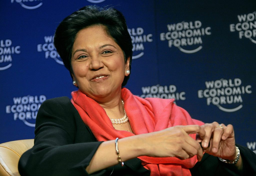 Indra Nooyi in a dark jacket and red scarf smiling at the World Economic Forum