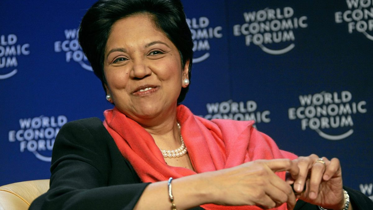 Indra Nooyi in a dark jacket and red scarf smiling at the World Economic Forum