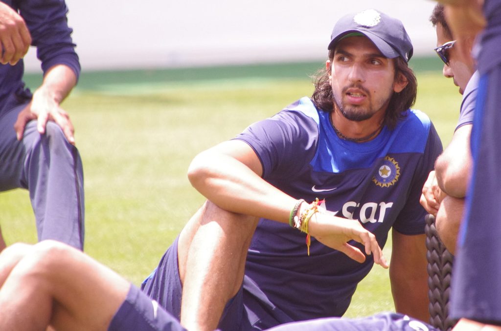 Ishant Sharma with long hair in a blue training shirt, sitting on the grass