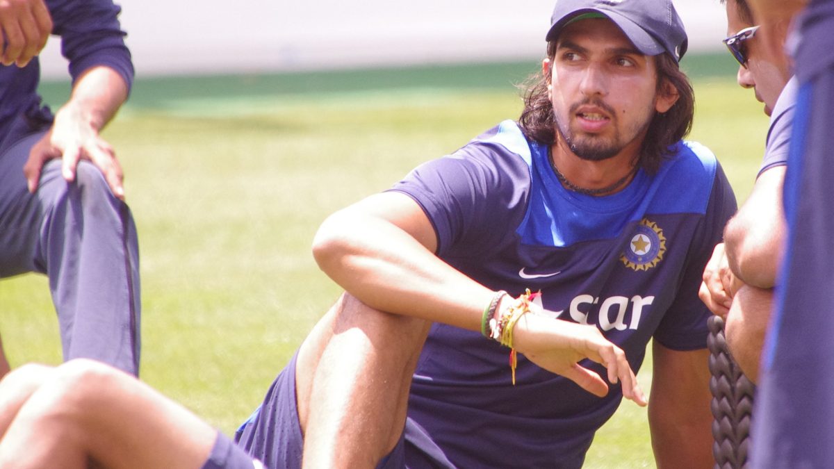 Ishant Sharma with long hair in a blue training shirt, sitting on the grass