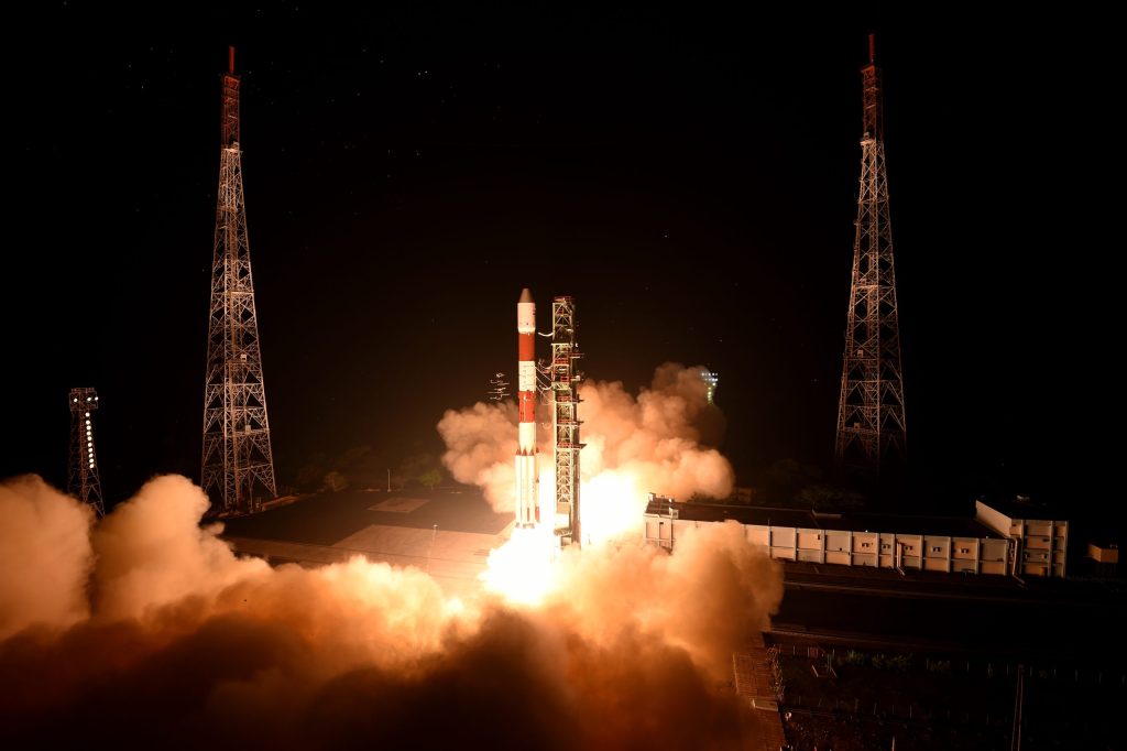 An ISRO PSLV rocket lifting off at night amid clouds of smoke