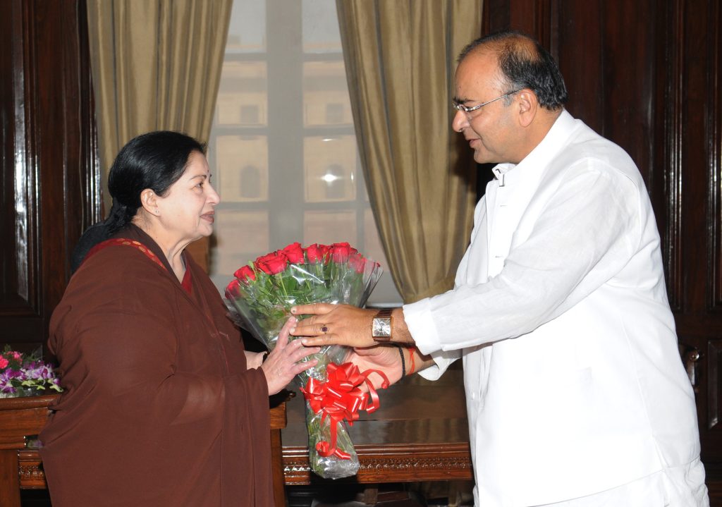 J. Jayalalithaa in a maroon sari receiving a bouquet from Finance Minister Arun Jaitley