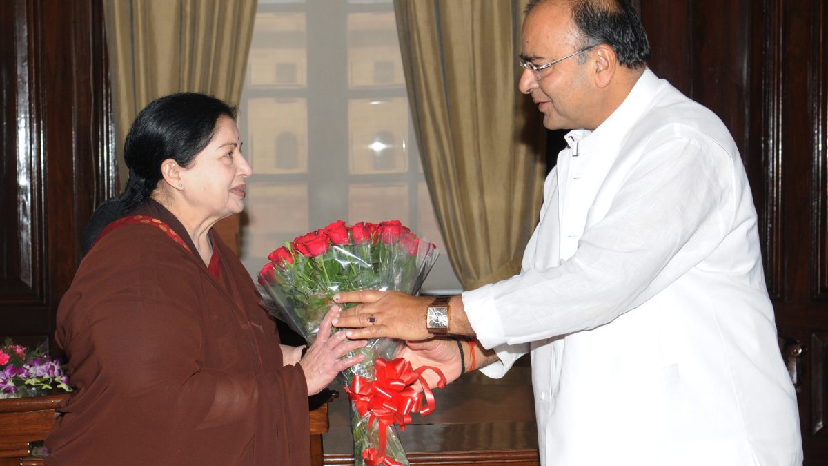 J. Jayalalithaa in a maroon sari receiving a bouquet from Finance Minister Arun Jaitley