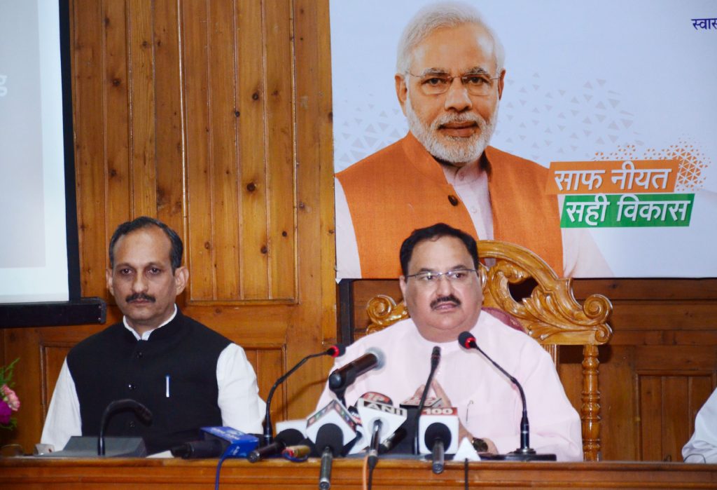 J. P. Nadda in glasses and a waistcoat speaking into press microphones beside another man