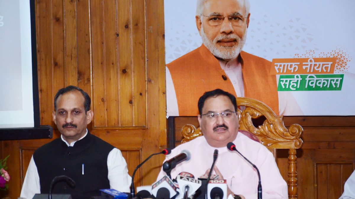 J. P. Nadda in glasses and a waistcoat speaking into press microphones beside another man
