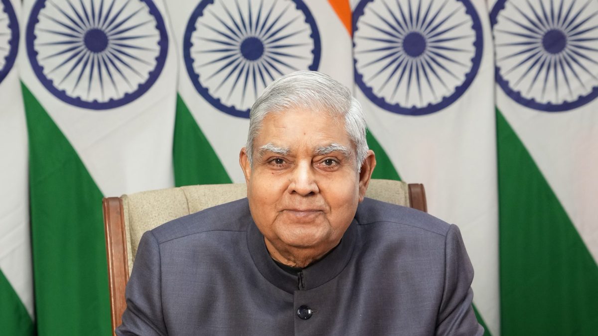 Jagdeep Dhankhar in a grey bandhgala seated in front of Indian national flags
