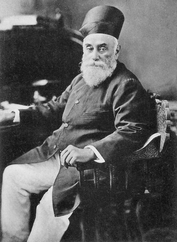 A portrait of Jamsetji Tata with a white beard, in a Parsi cap and coat