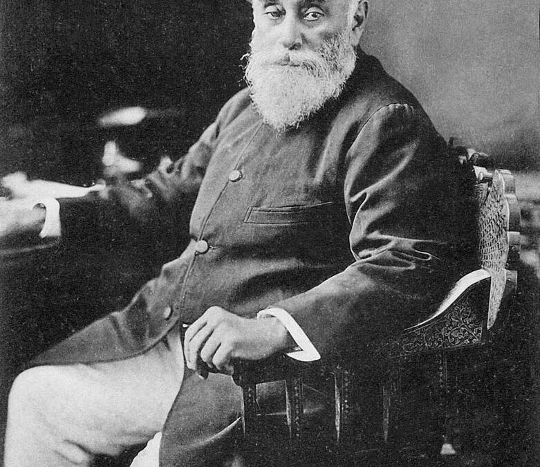 A portrait of Jamsetji Tata with a white beard, in a Parsi cap and coat