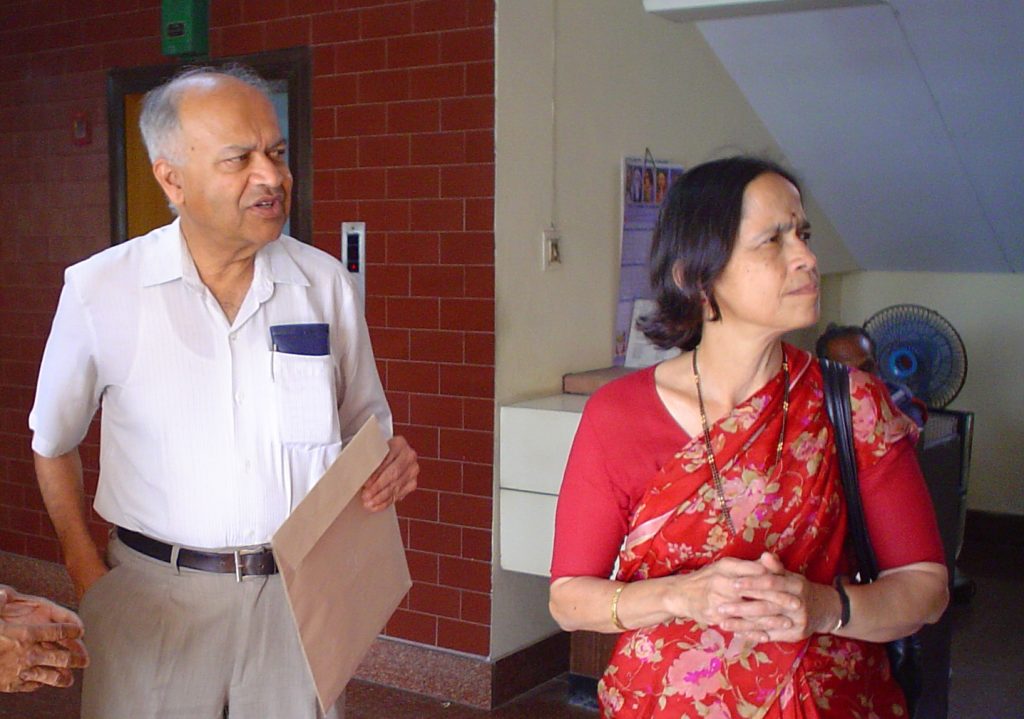 Jayant Narlikar in a white shirt standing beside his wife Mangala Narlikar in a red sari