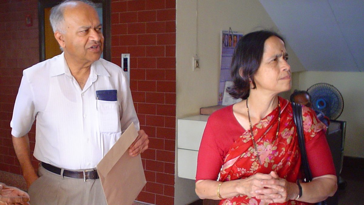 Jayant Narlikar in a white shirt standing beside his wife Mangala Narlikar in a red sari