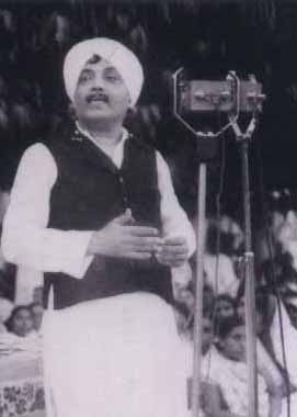 A black-and-white photograph of Jhaverchand Meghani in a turban, speaking before a microphone