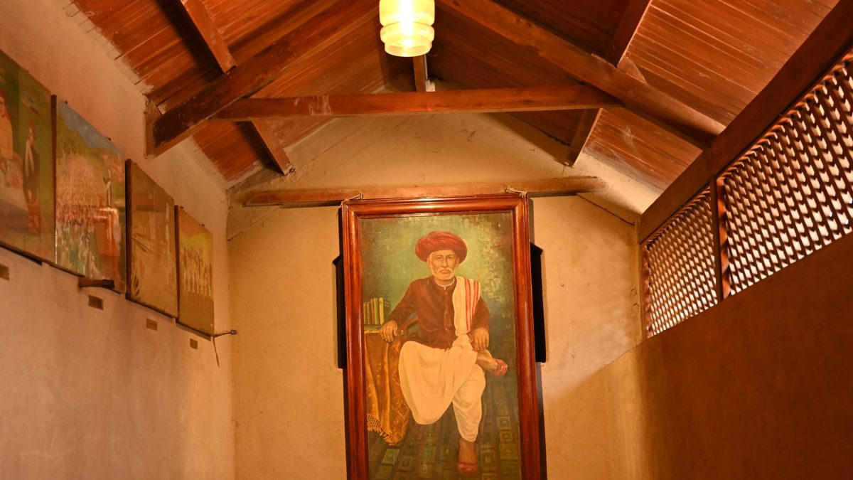 A framed painted portrait of Jyotirao Phule hanging in a wooden-roofed room