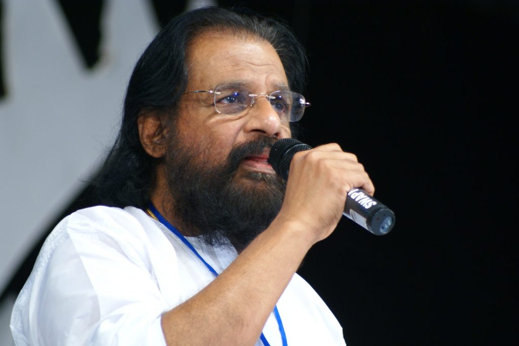 K. J. Yesudas with a white beard and glasses singing into a microphone