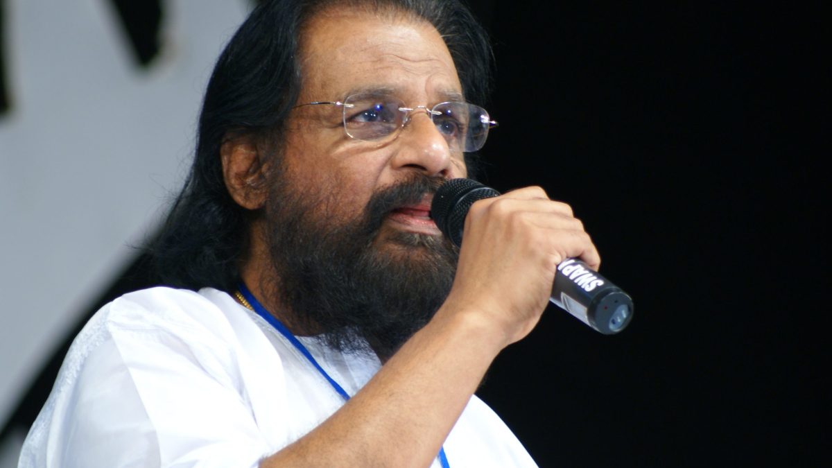 K. J. Yesudas with a white beard and glasses singing into a microphone