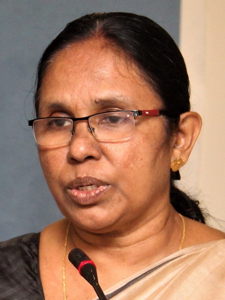 K. K. Shailaja in glasses speaking into a microphone