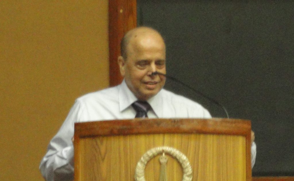 K. Kasturirangan in a white shirt speaking at a wooden lectern