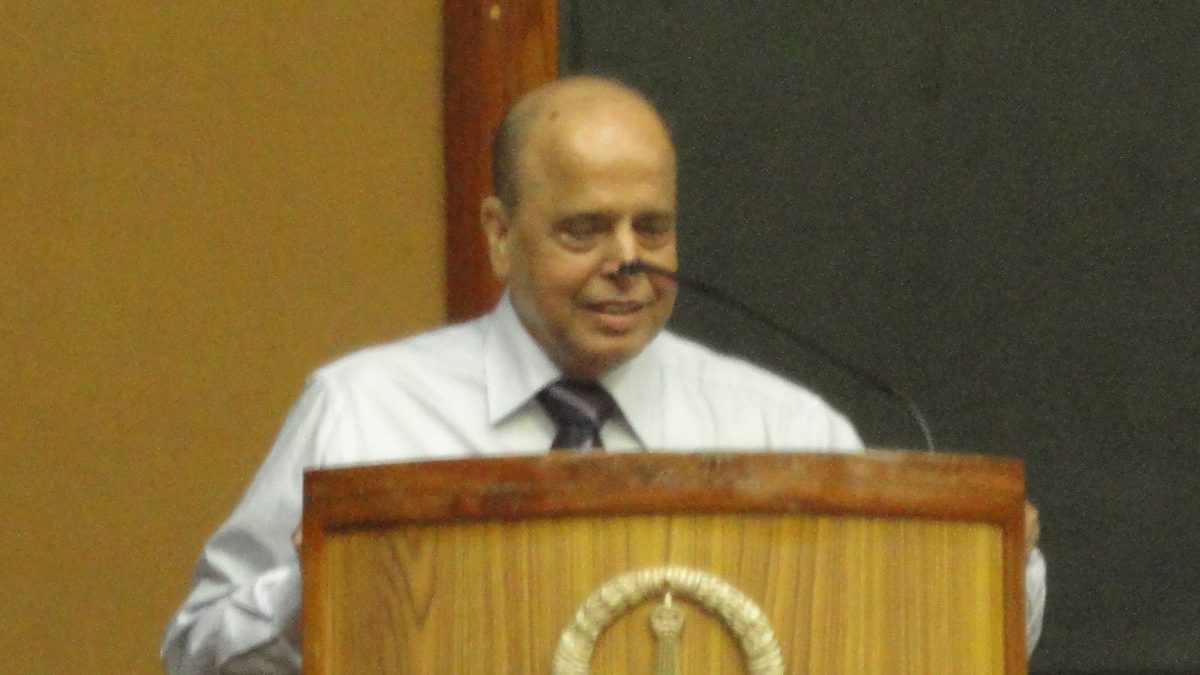 K. Kasturirangan in a white shirt speaking at a wooden lectern