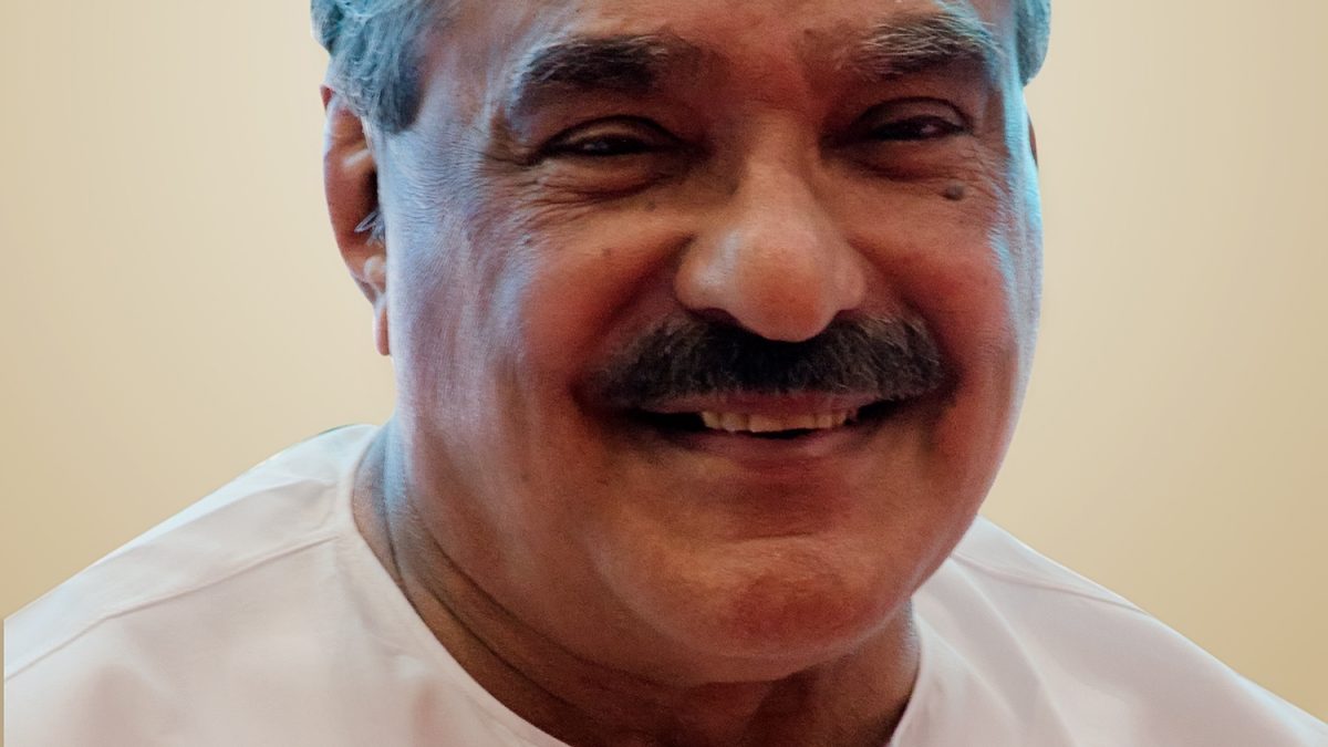 K. M. Mani with white hair and a moustache, smiling, in a white shirt