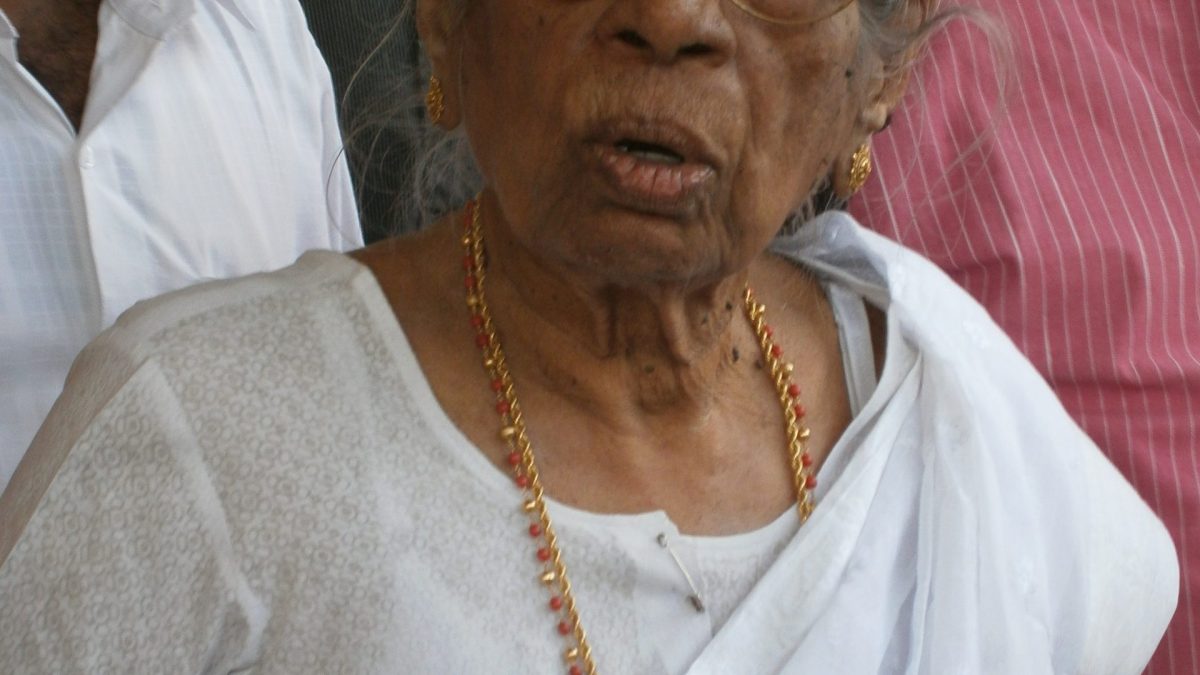 K. R. Gouri Amma in glasses and a white sari, wearing a rosette
