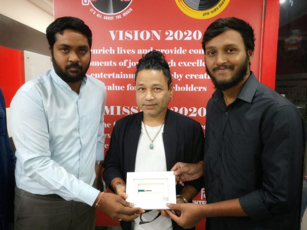 Kailash Kher in a white shirt and dark jacket standing between two young men at an event