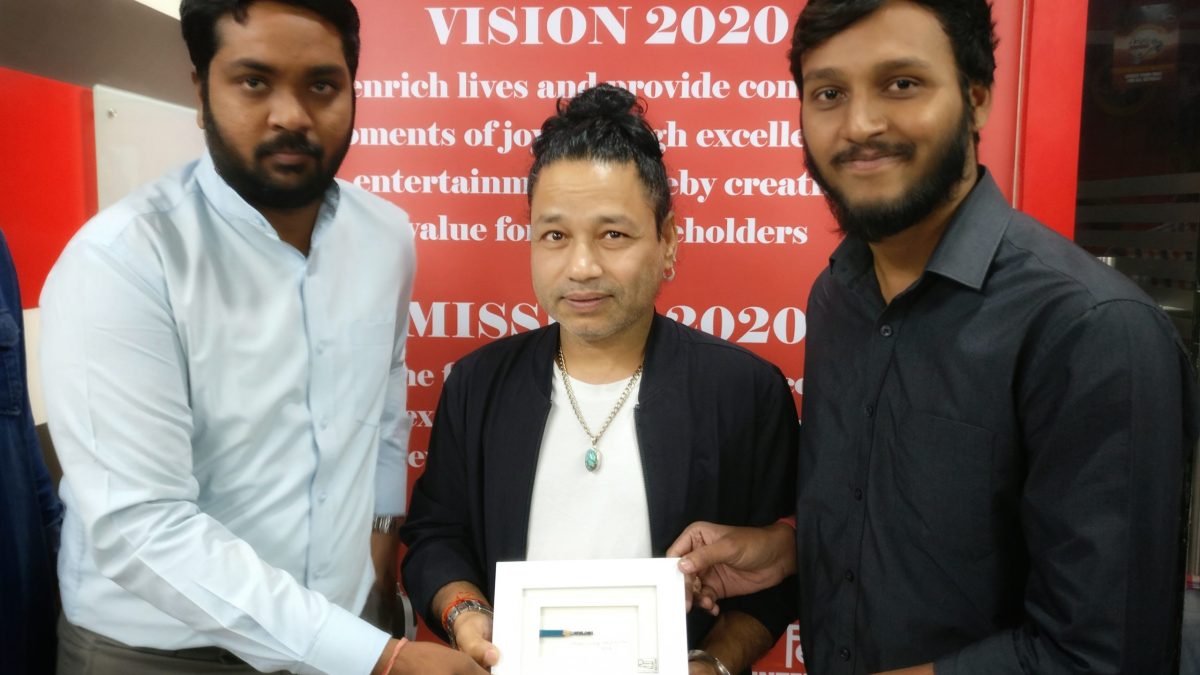 Kailash Kher in a white shirt and dark jacket standing between two young men at an event