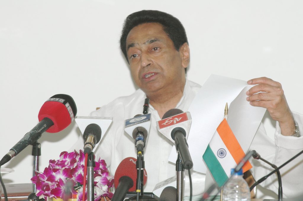 Kamal Nath in a white kurta gesturing as he speaks at press microphones