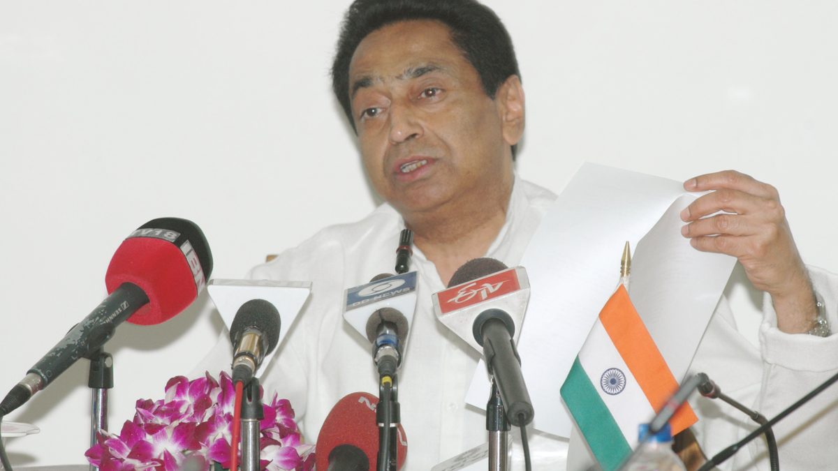 Kamal Nath in a white kurta gesturing as he speaks at press microphones