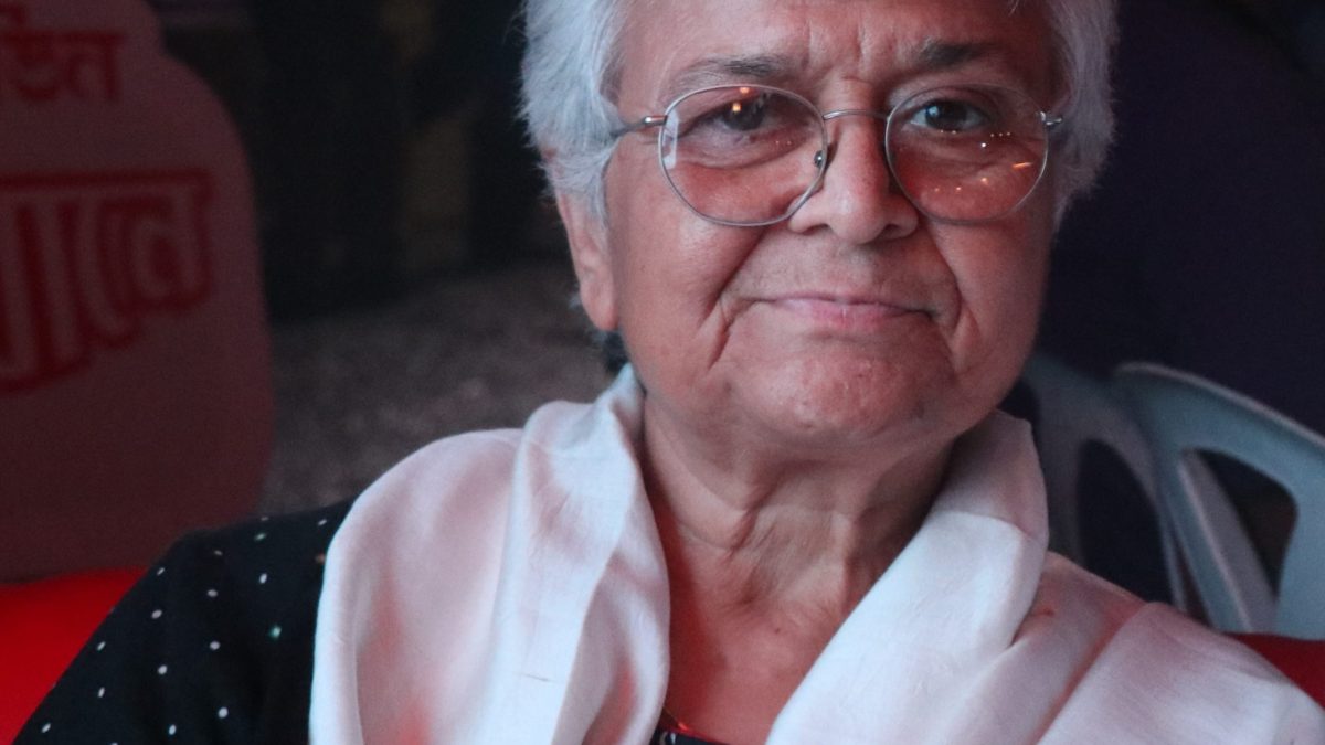 Kamla Bhasin with short white hair and glasses, a white and red shawl over her shoulders
