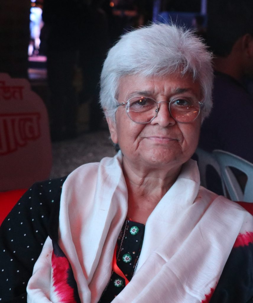 Kamla Bhasin with short white hair and glasses, a white and red shawl over her shoulders