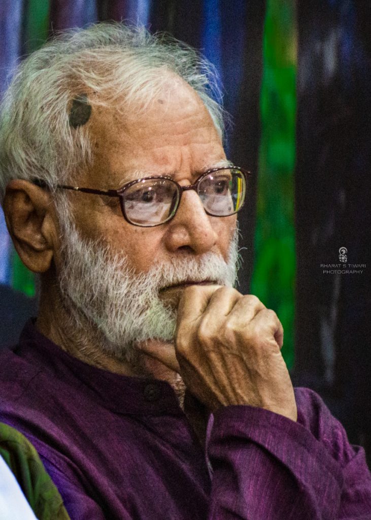 Kashinath Singh with a white beard and glasses, resting his chin on his hand