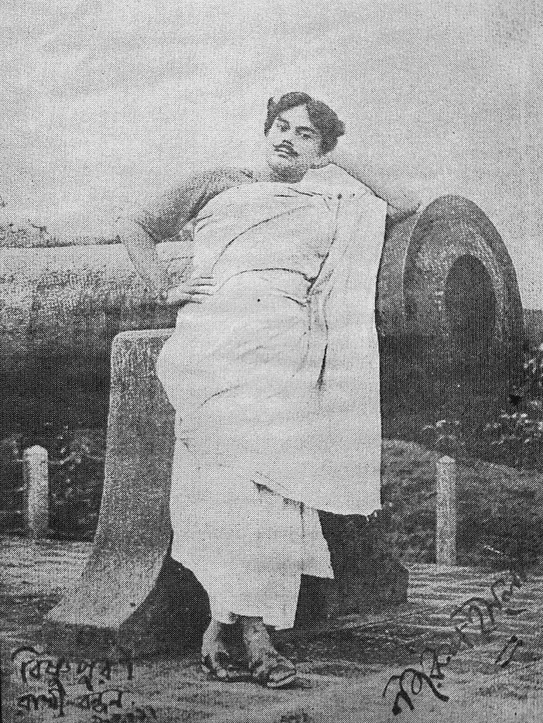 A young Kazi Nazrul Islam in a dhoti and shawl leaning against an old cannon