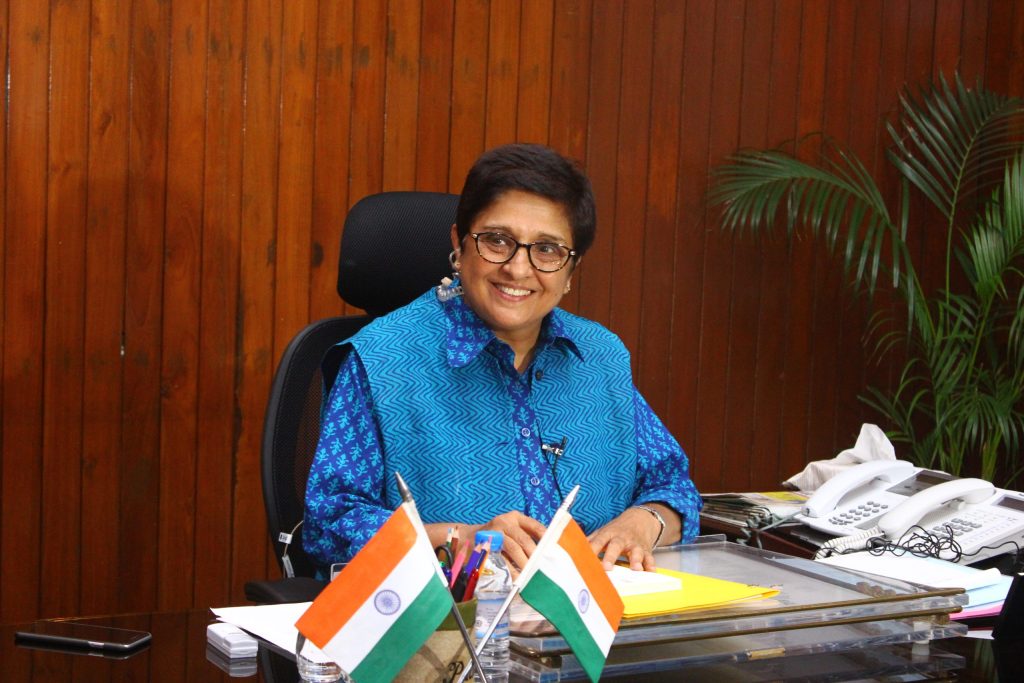 Kiran Bedi in a blue kurta smiling at her desk with Indian flags