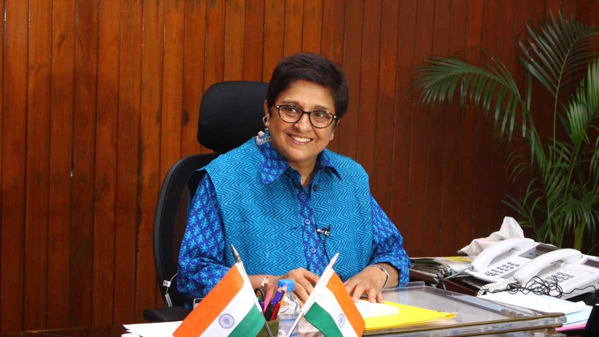 Kiran Bedi in a blue kurta smiling at her desk with Indian flags
