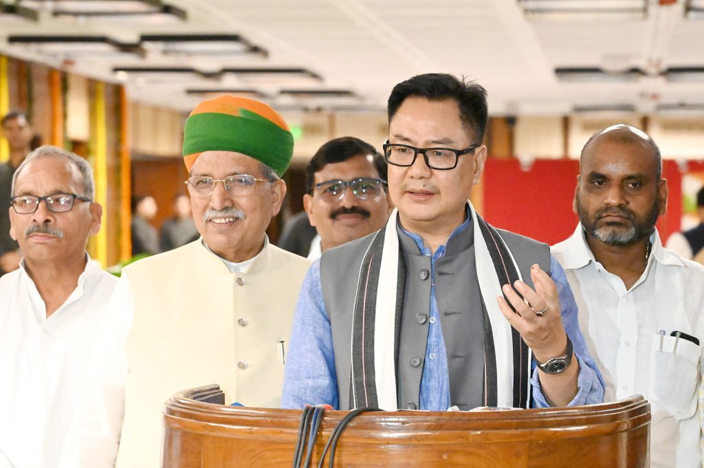 Kiren Rijiju in a dark jacket speaking to the media with other ministers beside him