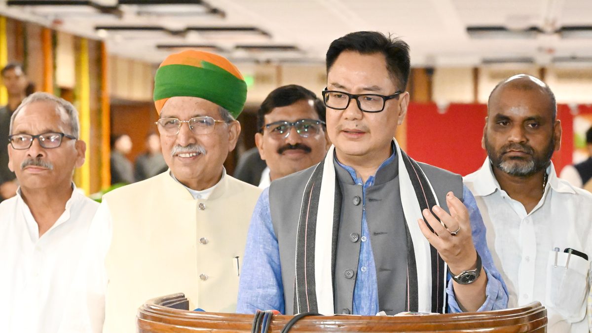 Kiren Rijiju in a dark jacket speaking to the media with other ministers beside him