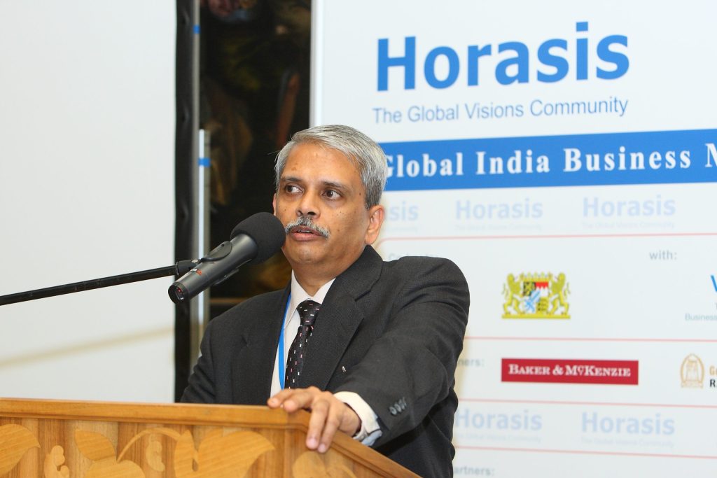 Kris Gopalakrishnan in glasses and a dark suit speaking at a lectern