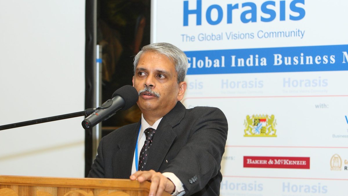 Kris Gopalakrishnan in glasses and a dark suit speaking at a lectern