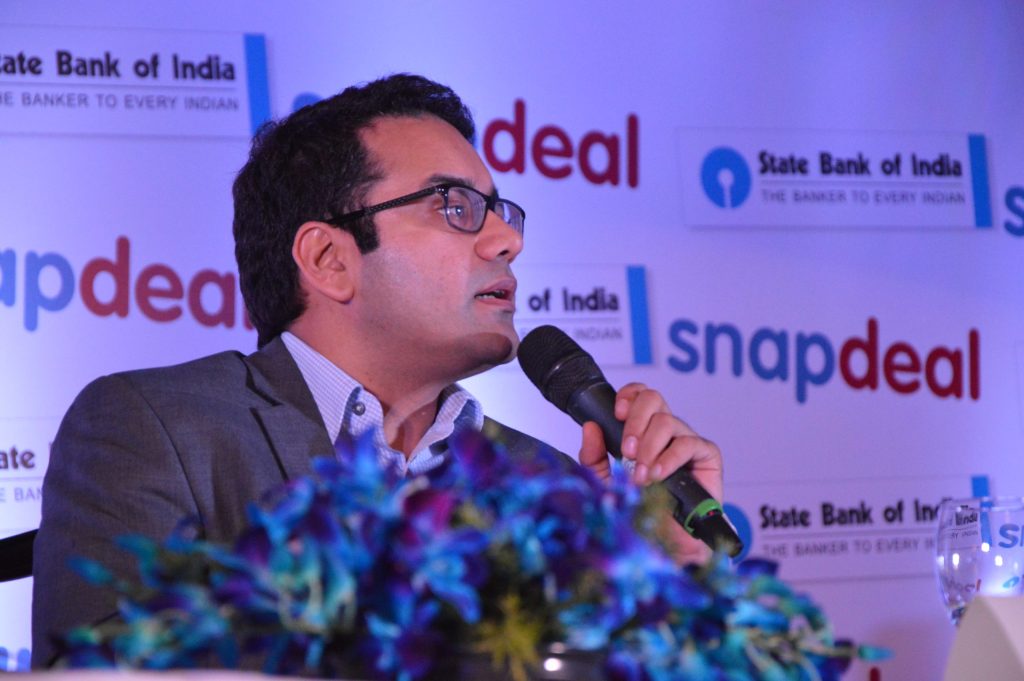 Kunal Bahl in glasses and a grey jacket speaking into a microphone at a Snapdeal event