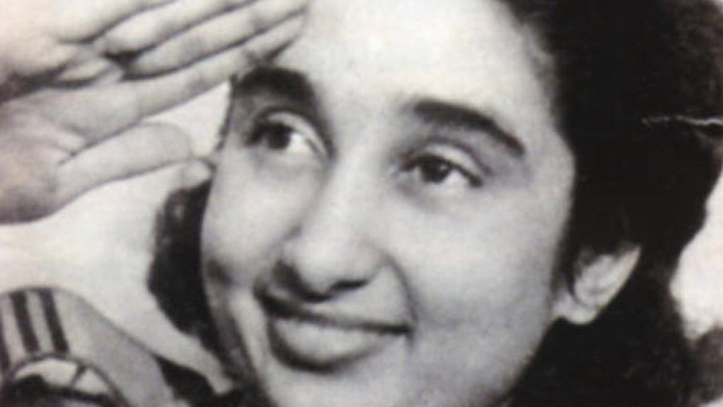 Black-and-white close-up of a young Lakshmi Sahgal smiling and saluting