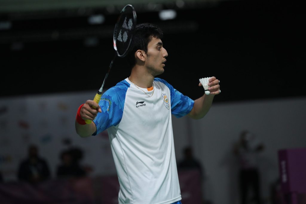 Lakshya Sen in a white and blue India shirt holding a shuttlecock, about to serve
