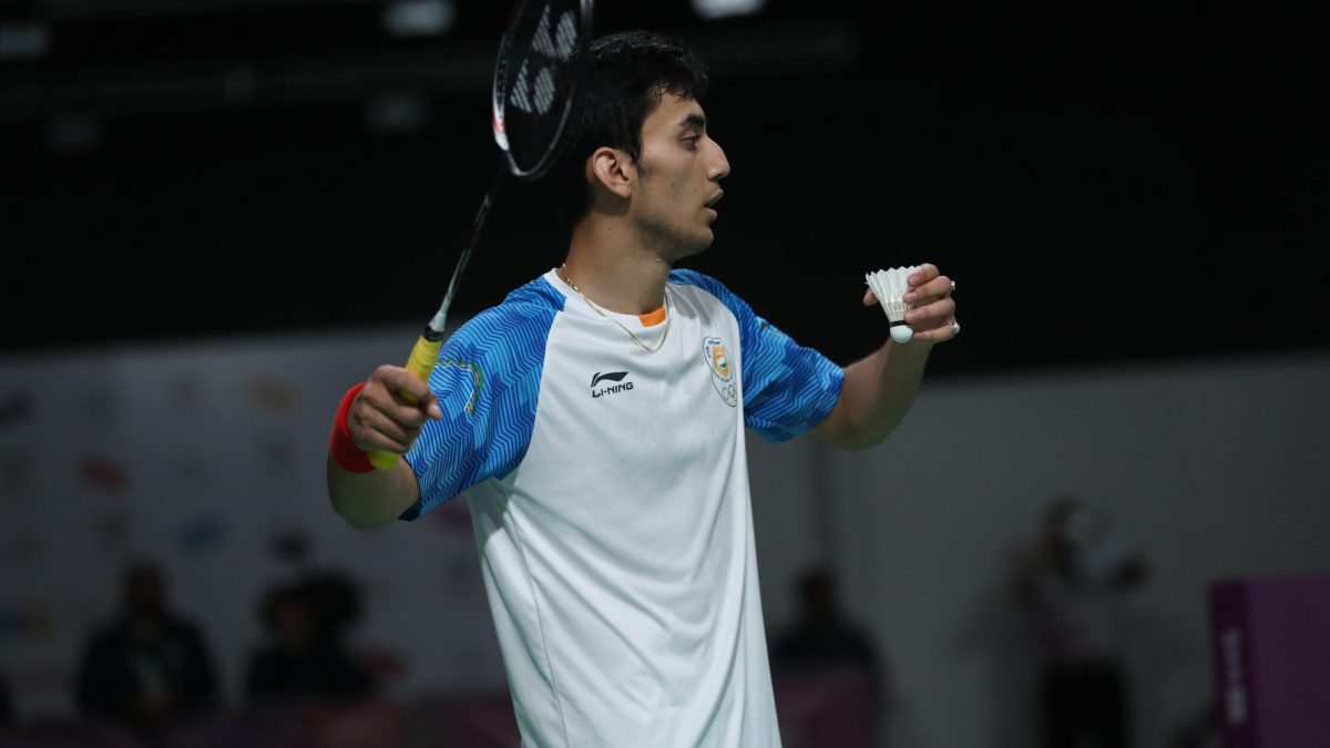 Lakshya Sen in a white and blue India shirt holding a shuttlecock, about to serve