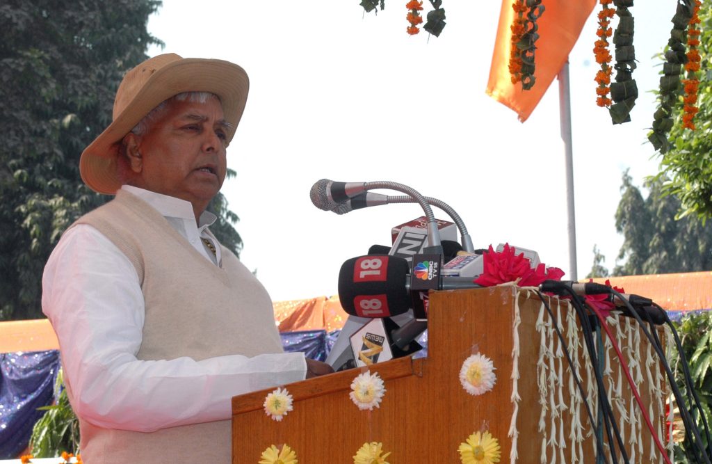 Lalu Prasad Yadav in a hat and waistcoat speaking at a decorated lectern