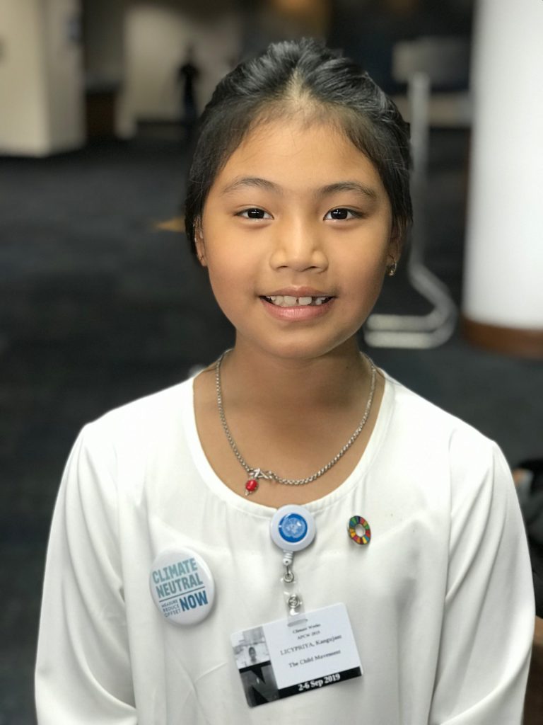 Licypriya Kangujam, aged seven, smiling in a white top with conference badges