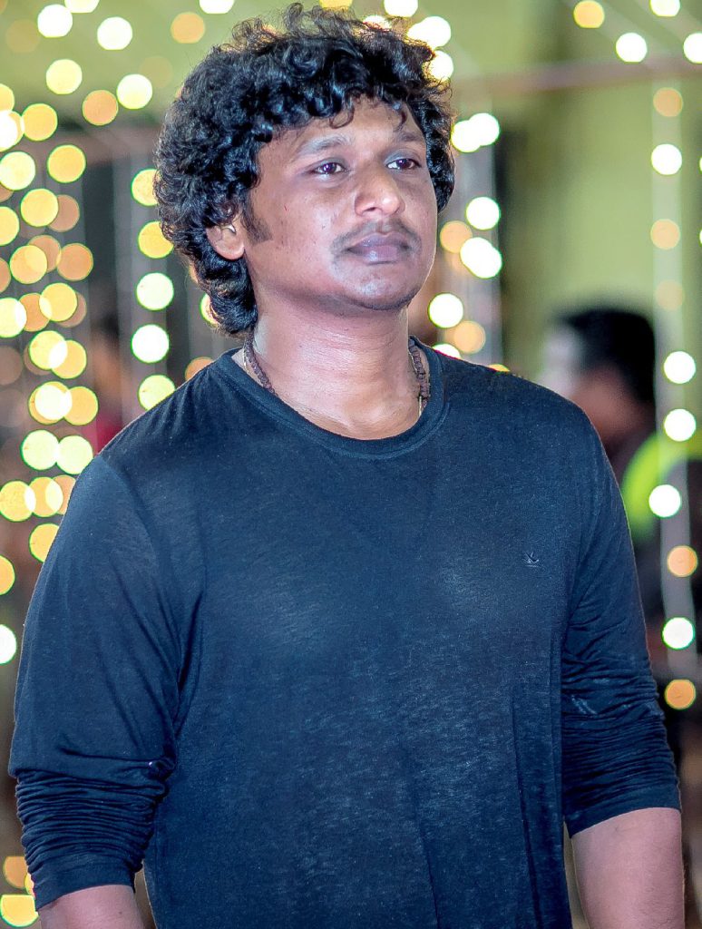 Lokesh Kanagaraj with curly hair, in a blue sweatshirt, at an awards event