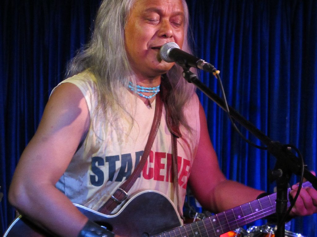 Lou Majaw with long white hair playing a guitar on stage