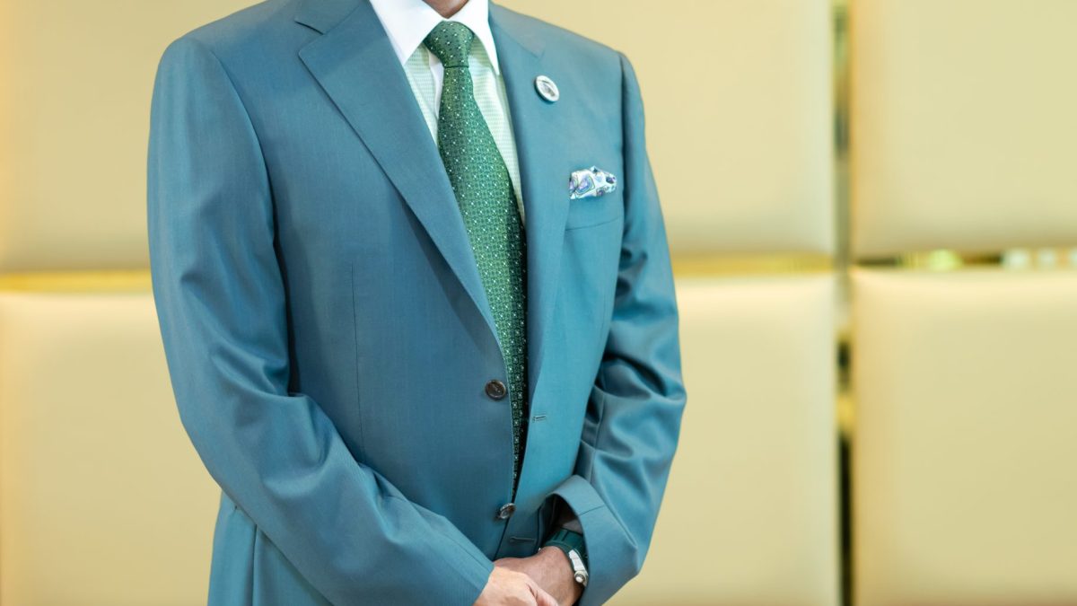 M. A. Yusuff Ali standing in a green suit in the lobby of his office