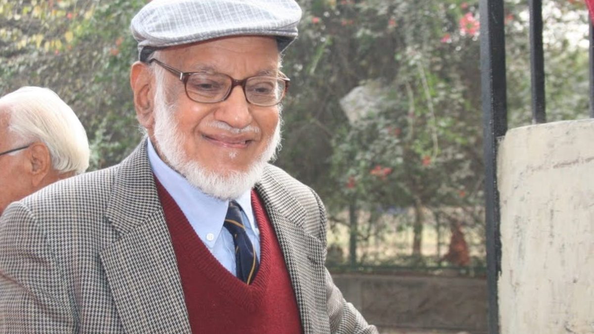 An elderly M. G. K. Menon with a white beard and glasses, wearing a cap and a tweed jacket