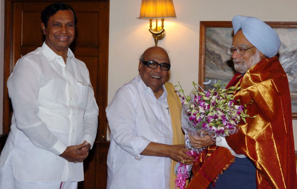 M. Karunanidhi in dark glasses and a yellow shawl greeting Prime Minister Manmohan Singh with flowers