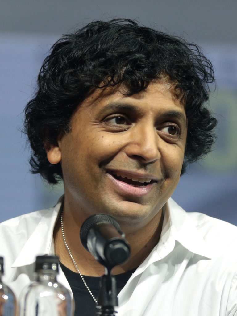 M. Night Shyamalan smiling as he speaks into a microphone